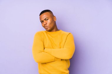 Mor arka planda izole olmuş, hoşnutsuzca kaşlarını çatan, kollarını kavuşturan genç Latin bir adam..