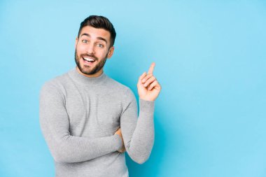 Mavi arka planda genç, beyaz bir adam izole edilmiş, mutlu bir şekilde işaret parmağıyla işaret ediyor..