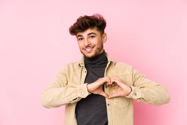 Arka planda poz veren genç bir Arap adam izole edilmiş gülümsüyor ve elleriyle kalp şekli gösteriyor..