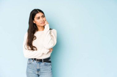 Mavi arka planda izole edilmiş genç Hintli kadın üzgün ve dalgın hissediyor, kopyalama alanına bakıyor..
