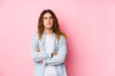 Uzun saçlı adam kendini soyutlamış gülümsüyor ve kollarını kavuşturuyor..