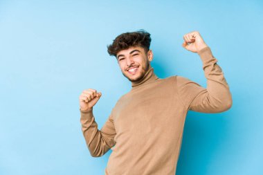 Genç Arap adam özel bir günü kutluyor, atlıyor ve enerjiyle kollarını kaldırıyor..