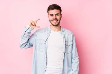 Beyaz arka planda poz veren beyaz tenli genç bir iş adamı. Elinde işaret parmaklarıyla küçük bir şey tutuyor, gülümsüyor ve kendinden emin..