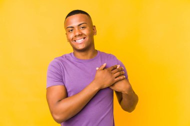 Sarı arka planda izole edilmiş genç latin adam, avuçlarını göğsüne bastıran dostça bir ifadeye sahiptir. Aşk konsepti.