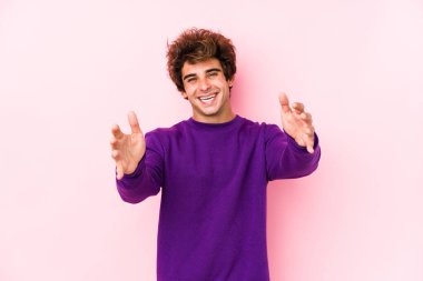 Pembe arka planı olan genç beyaz bir adam kameraya sarıldığı için kendini güvende hissediyor..