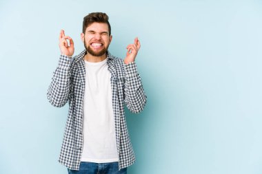 Kafkasyalı genç adam mavi arka planda izole edilmiş şans dilemek için şans diliyor.