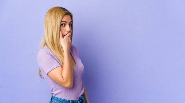 Mor arka planda izole edilmiş genç sarışın bir kadın. Bir fotokopi odasına dikkatlice bakıyor. Ağzını eliyle kapatıyor..