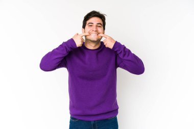 Beyaz arka planda izole edilmiş genç adam gülümsüyor, parmaklarını ağzına doğrultuyor..