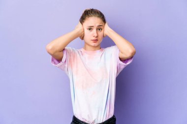 Mor arka planda genç beyaz bir kadın. Kulaklarını elleriyle kapatıyor. Gürültülü sesler duymamaya çalışıyor..