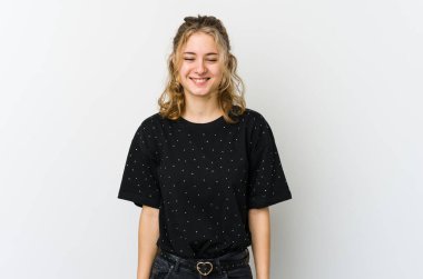 Beyaz arka plandaki genç beyaz kadın gülüyor ve gözlerini kapatıyor, rahatlamış ve mutlu hissediyor..