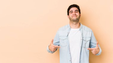 Bej arka planda yaşayan genç bir adam gömlek fotokopi alanını elle işaret ediyor, gururlu ve kendinden emin.