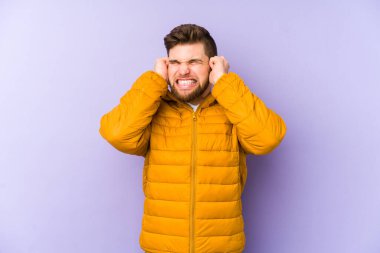 Mor arka planda izole edilmiş genç adam kulakları elleriyle kapatıyor..
