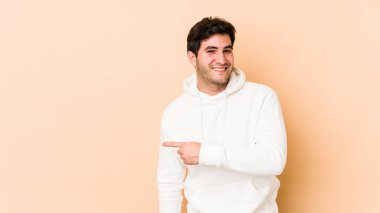 Bej arka planda izole edilmiş genç bir adam gülümsüyor ve boş alanda bir şeyler gösteriyor..
