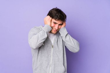 Mor arka planda izole edilmiş genç adam kulakları elleriyle kapatıyor..
