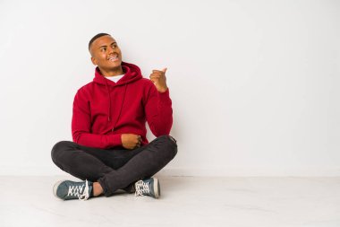 Yerde oturan genç latin adam, parmak kadar uzakta izole noktalar, gülüyor ve kaygısız.