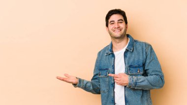 Bej arka planda izole edilmiş genç bir adam heyecanlı bir şekilde avuç içinde bir kopya alanı tutuyor..