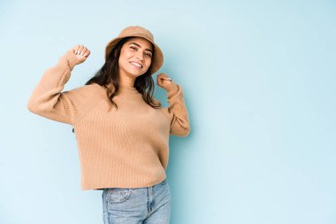 Mavi arka planda izole edilmiş bir şapka takan genç Hintli kadın özel bir günü kutluyor, atlıyor ve enerji ile kollarını kaldırıyor..