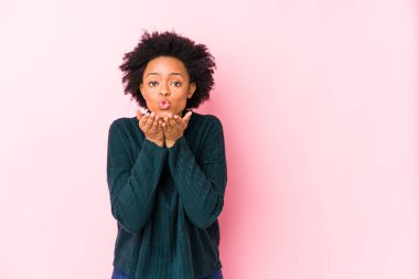 Orta yaşlı Afrikalı Amerikalı bir kadın pembe bir arka plana karşı izole edilmiş dudaklar ve hava öpücüğü göndermek için avuç içleri tutuyor..