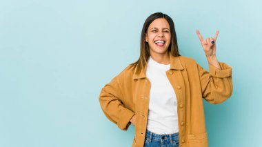 Mavi arka planda izole edilmiş genç bir kadın parmaklarıyla kaya hareketi gösteriyor.