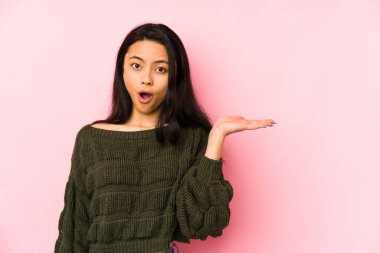 Pembe arka planda izole edilmiş genç Çinli kadın, avuç içi fotokopi alanını elinde tutmaktan etkilenmiş..