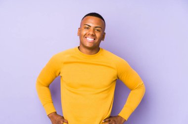 Mor arka planda izole edilmiş genç latin adam ellerini kalçasında tutuyor..