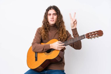 Genç beyaz adam gitar çalıyor. İki numarayı parmaklarıyla gösteriyor..