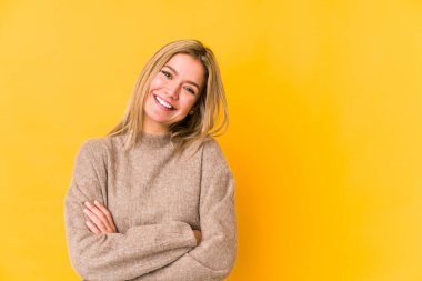 Sarışın, beyaz tenli, soyutlanmış, kollarını kavuşturarak gülümseyen bir kadın..