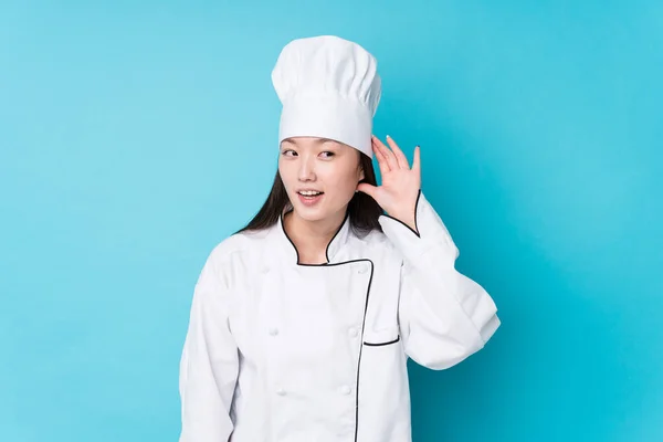 Young chinese chef woman isolated trying to listening a gossip.