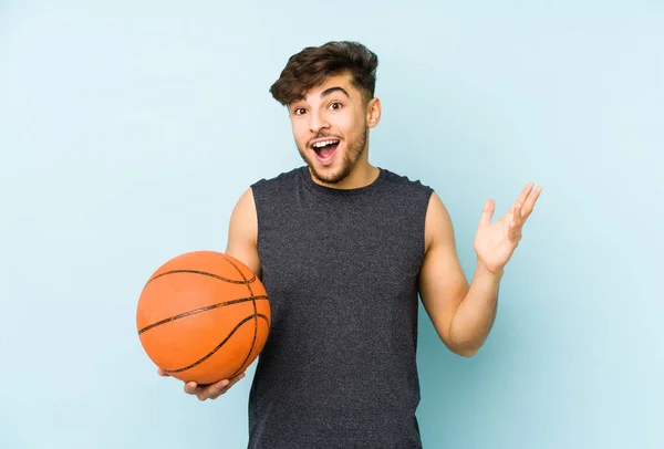 Young arabian man playing basket isolated receiving a pleasant surprise, excited and raising hands.