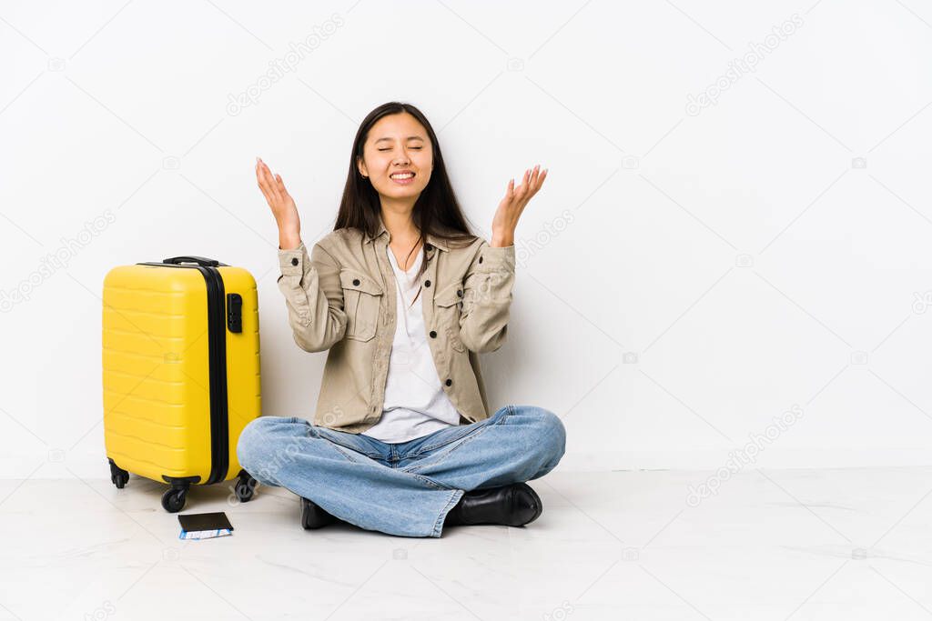 Young chinese traveler woman sitting holding a boarding passes screaming to the sky, looking up, frustrated.