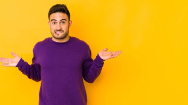 Kafkasyalı genç adam sarı fırında izole edilmiş. Kafası karışmış ve omuz silkiyor. Kopya alanını tutmak için..