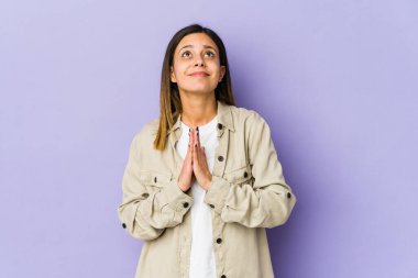 Mor arka planda izole edilmiş genç bir kadın. El ele tutuşup, ağzının kenarında dua ediyor. Kendine güveniyor..