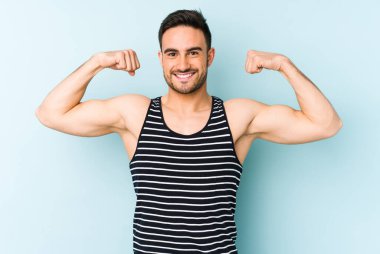 Mavi arka planda izole edilmiş genç beyaz adam güçlü bir hareket sergiliyor kollarıyla, kadınsı gücün sembolü.