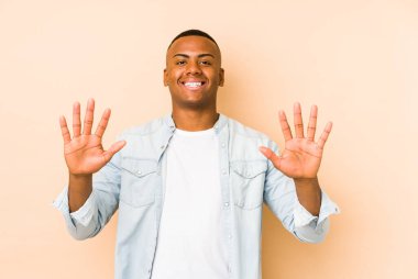 Bej arka planda izole edilmiş genç latin adam on numarayı elleriyle gösteriyor..