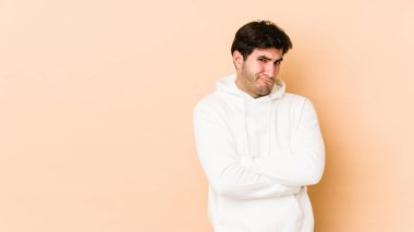 Bej arka planda izole genç adam hoşnutsuzca kaşlarını çatıyor, kollarını kavuşturuyor..