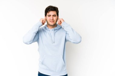 Genç adam beyaz arka planda kulaklarını parmaklarıyla kapatıyor. Yüksek sesli bir ortam yüzünden stresli ve çaresiz..