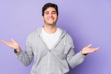 Mor arka planda izole edilmiş genç adam kollarıyla ölçek oluşturuyor, mutlu ve kendinden emin hissediyor..
