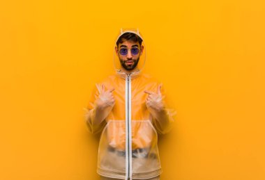 Yağmurluk giyen genç adam şaşırdı, başarılı ve başarılı hissediyor.