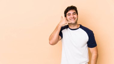Bej arka planda izole edilmiş genç bir adam parmakları olan bir cep telefonu hareketi gösteriyor..