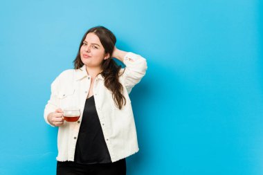 Genç kavisli kadın elinde çay fincanıyla kafasının arkasına dokunuyor, düşünüyor ve bir seçim yapıyor..