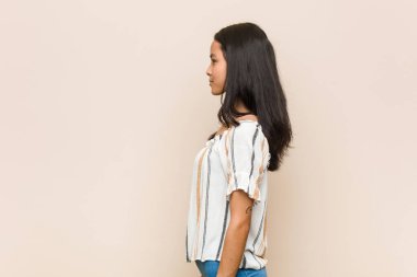 Genç sevimli Çinli genç sarışın kadın pembe bir arka plana karşı ceket giyiyor sola bakıyor, yan pozlar veriyor..