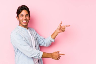 Pembe arka planda poz veren genç, beyaz bir adam..