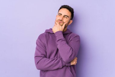 Kafkasyalı genç bir adam mor arka planda izole edilmiş düşünüyor, bakıyor, yansıtıyor, düşünüyor, bir fantezi kuruyor..