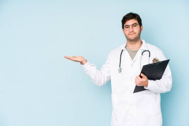 Mavi arka planda izole edilmiş genç bir doktor avucunun içinde bir kopya alanı olduğunu ve başka bir elin belinde olduğunu gösteriyor..