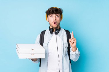 Elinde pizza tutan genç bir Arap öğrenci ağzı açık bir şekilde tepeyi işaret ediyor..