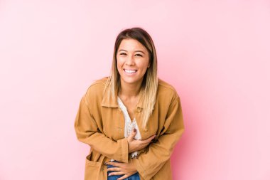 Yalnız poz veren beyaz bir kadın mutlu bir şekilde gülüyor ve ellerini karnının üstünde tutarak eğleniyor..