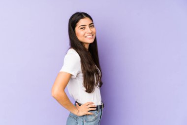 Mor arka planda izole edilmiş genç Hintli kadın ellerini kalçasından ayırmıyor..