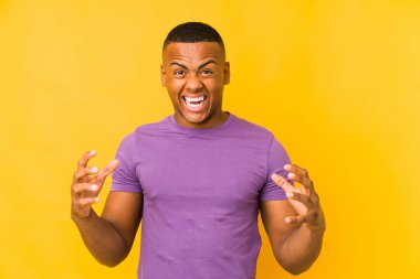 Sarı arka planda izole edilmiş genç Latin adam öfkeyle bağırıyor..