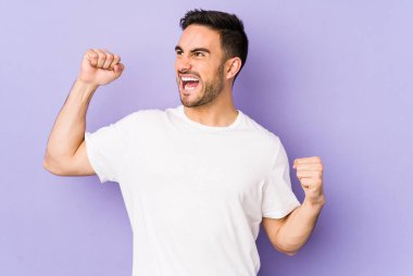 Mor arka planda izole edilmiş genç beyaz adam zafer kazandıktan sonra yumruğunu kaldırıyor, kazanan konsept..