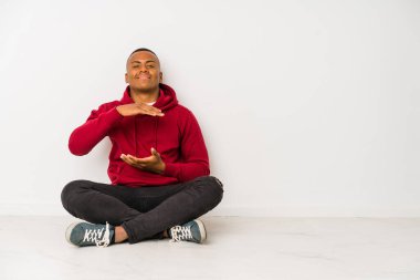 Yerde yalnız oturan genç latin adam iki eliyle bir şey tutuyor, ürün sunumu..